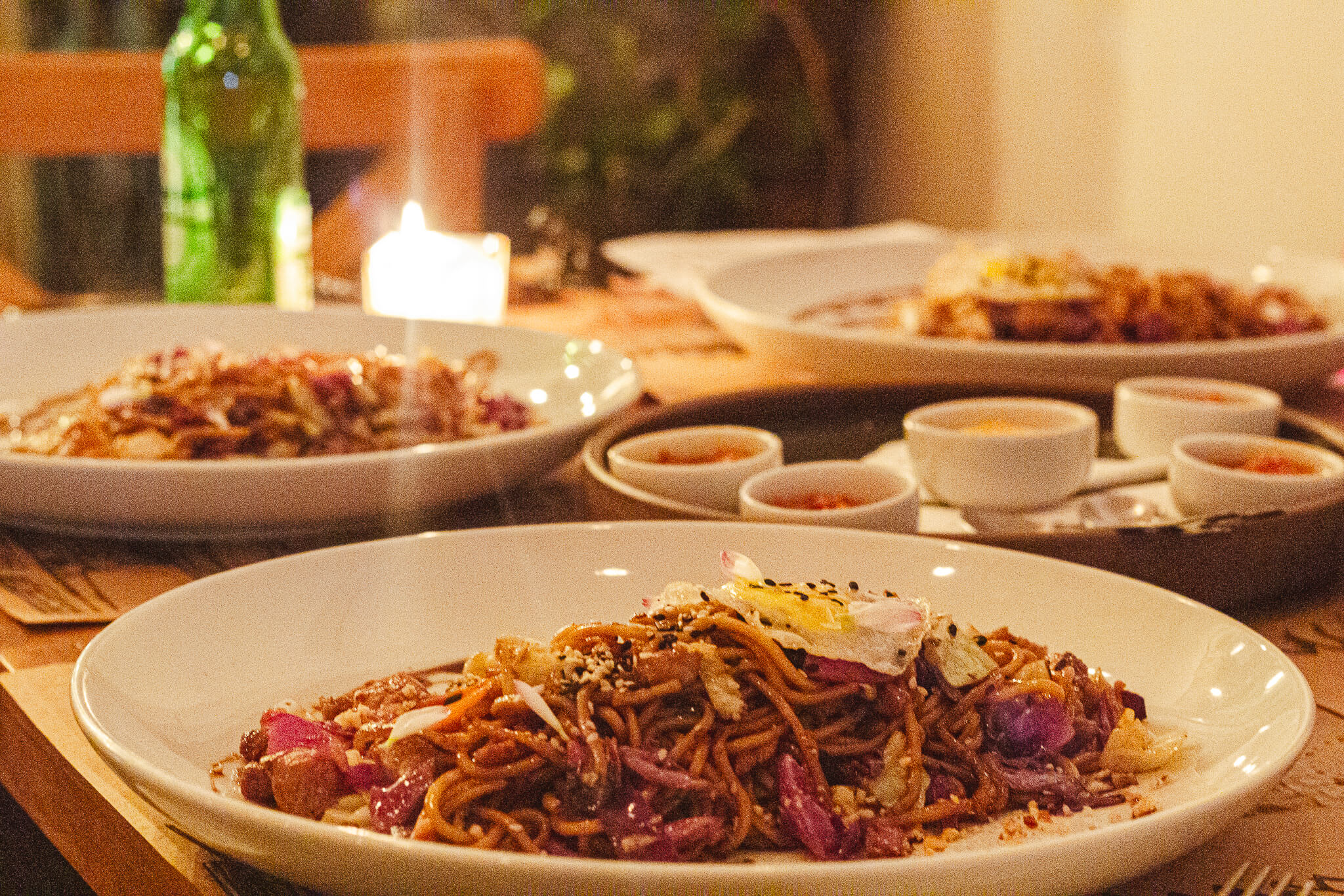 Mesa com três pratos de Mie Goreng, macarrão tradicional da indonésia e 3 potinhos de molho