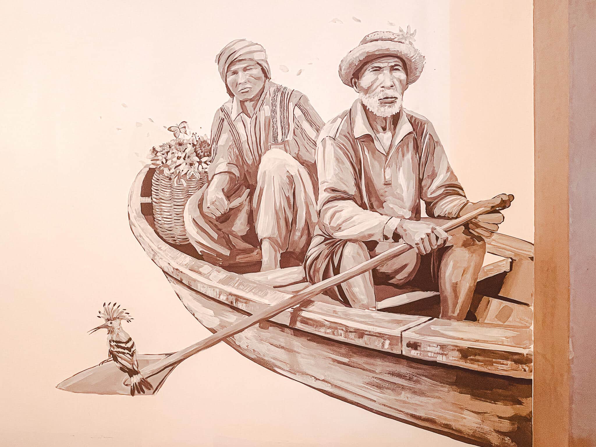 Ilustração na parede de duas pessoas em um barquinho a remo e um passarinho típico da Tailândia sentando na ponta do remo, quase na água.
