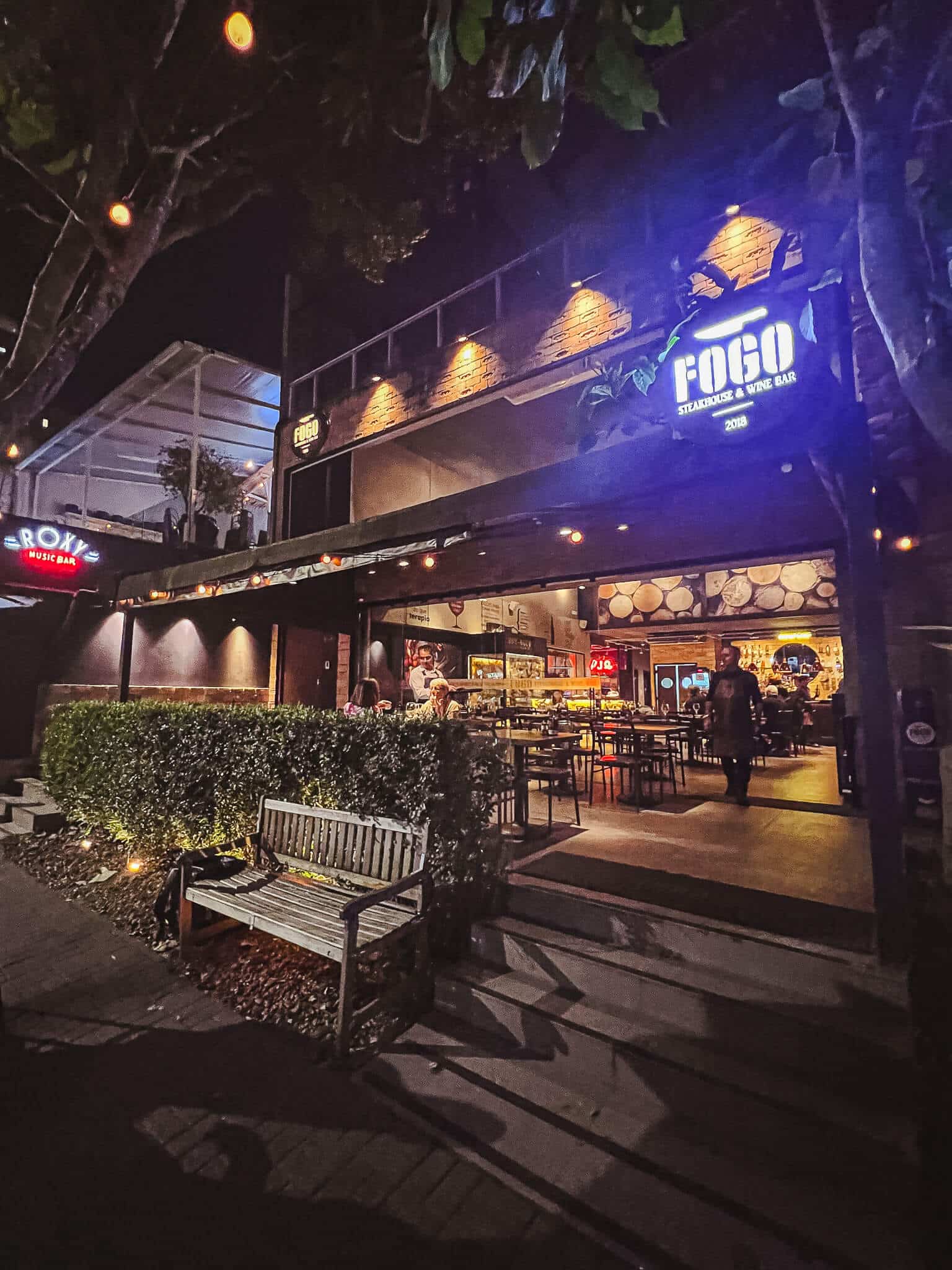 foto mostra a fachada do restaurante fogo steakhouse ao anoitecer, com o logo brilhando e luzes quentes iluminando