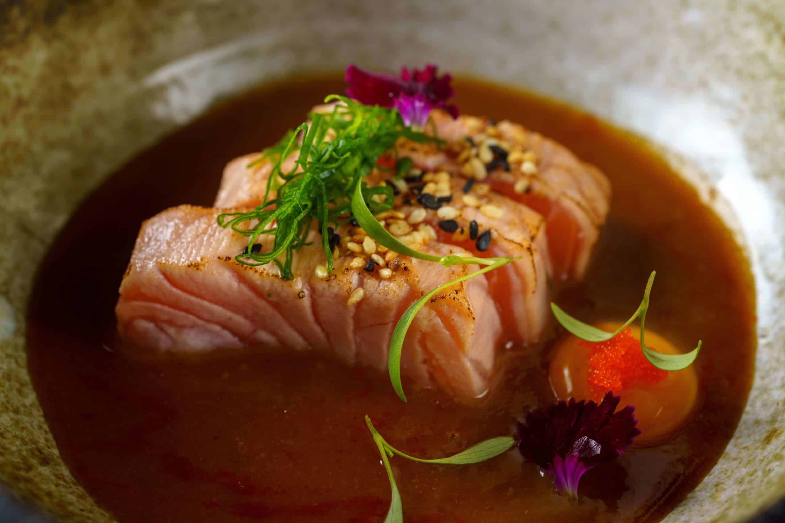 foto mostra um salmão ao maçarico, gema de codorna, gergelim, cebolinha com molho missô
