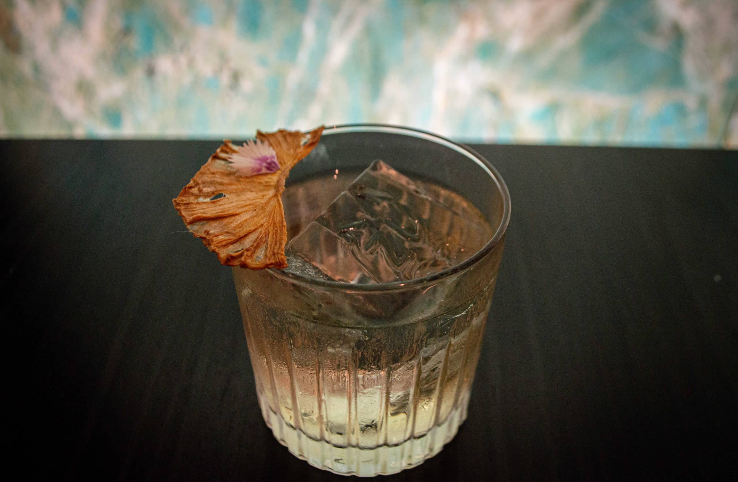 foto mostra um drink com um pedra de gelo estilizada com o nome kazuo dentro do drink.