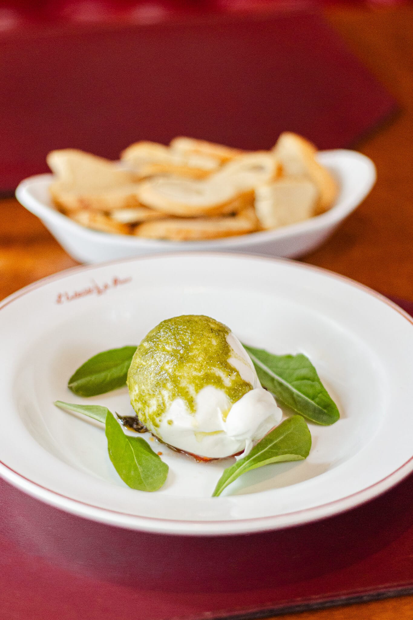 foto mostra uma burrata de bufala com molho pesto e torradinhas ao fundo