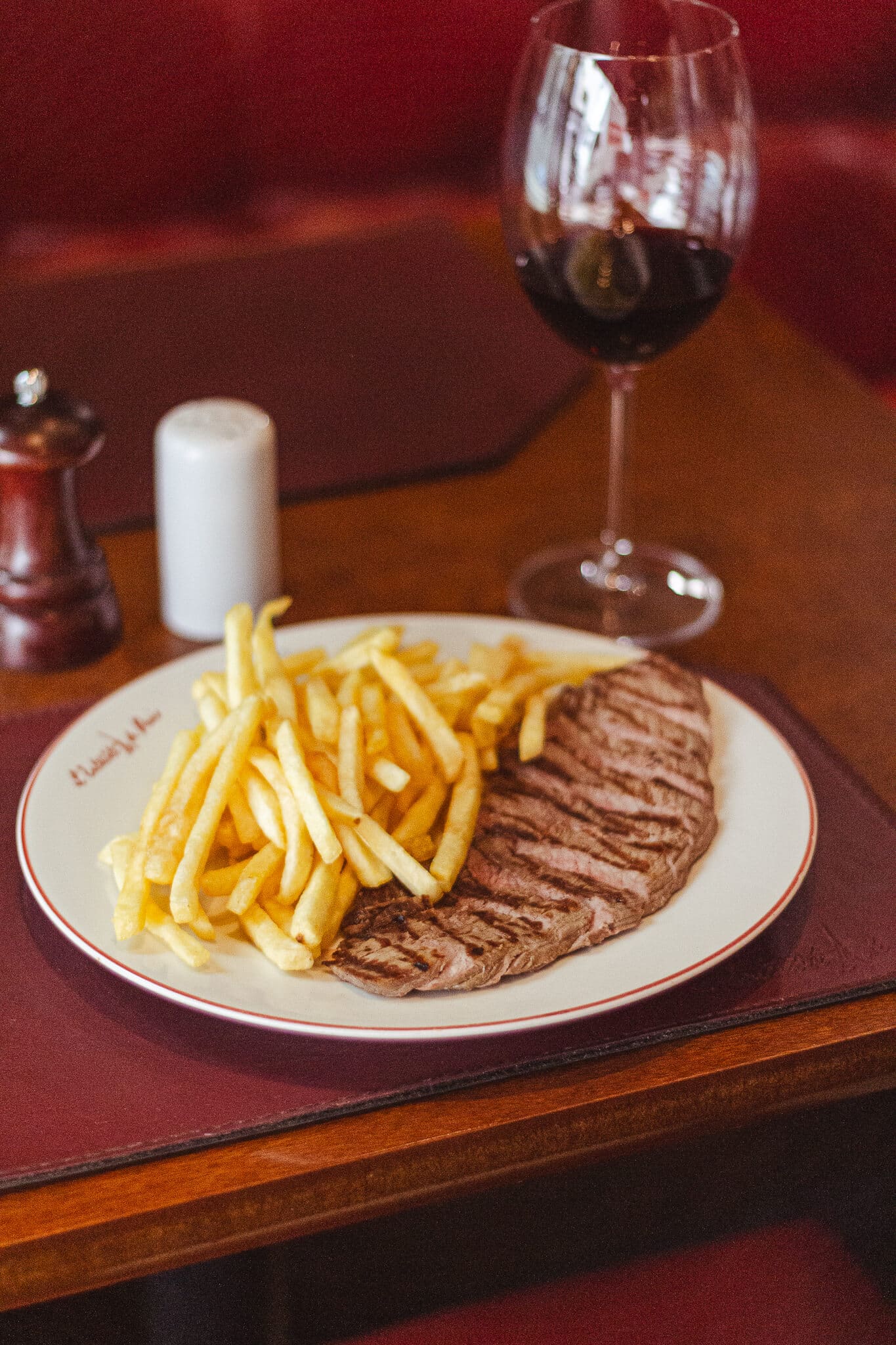 foto mostra um entrecote no prato ao lado de batatas fritas e uma taça de vinho