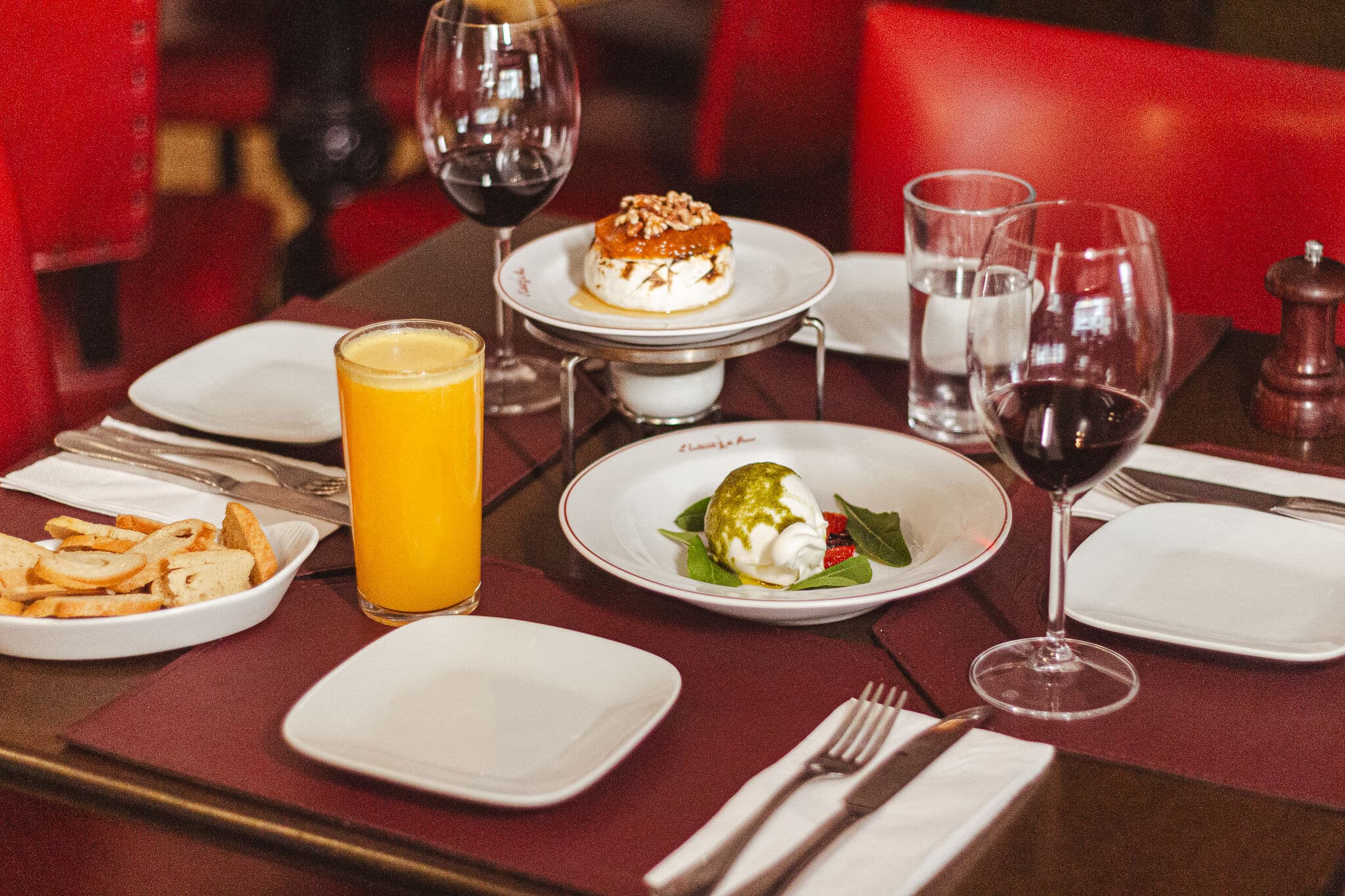 foto mostra a mesa posta com as entradas do restaurante, com o brie gratinado e burrata de bufala ao lado de um copo de suco e uma taça de vinho