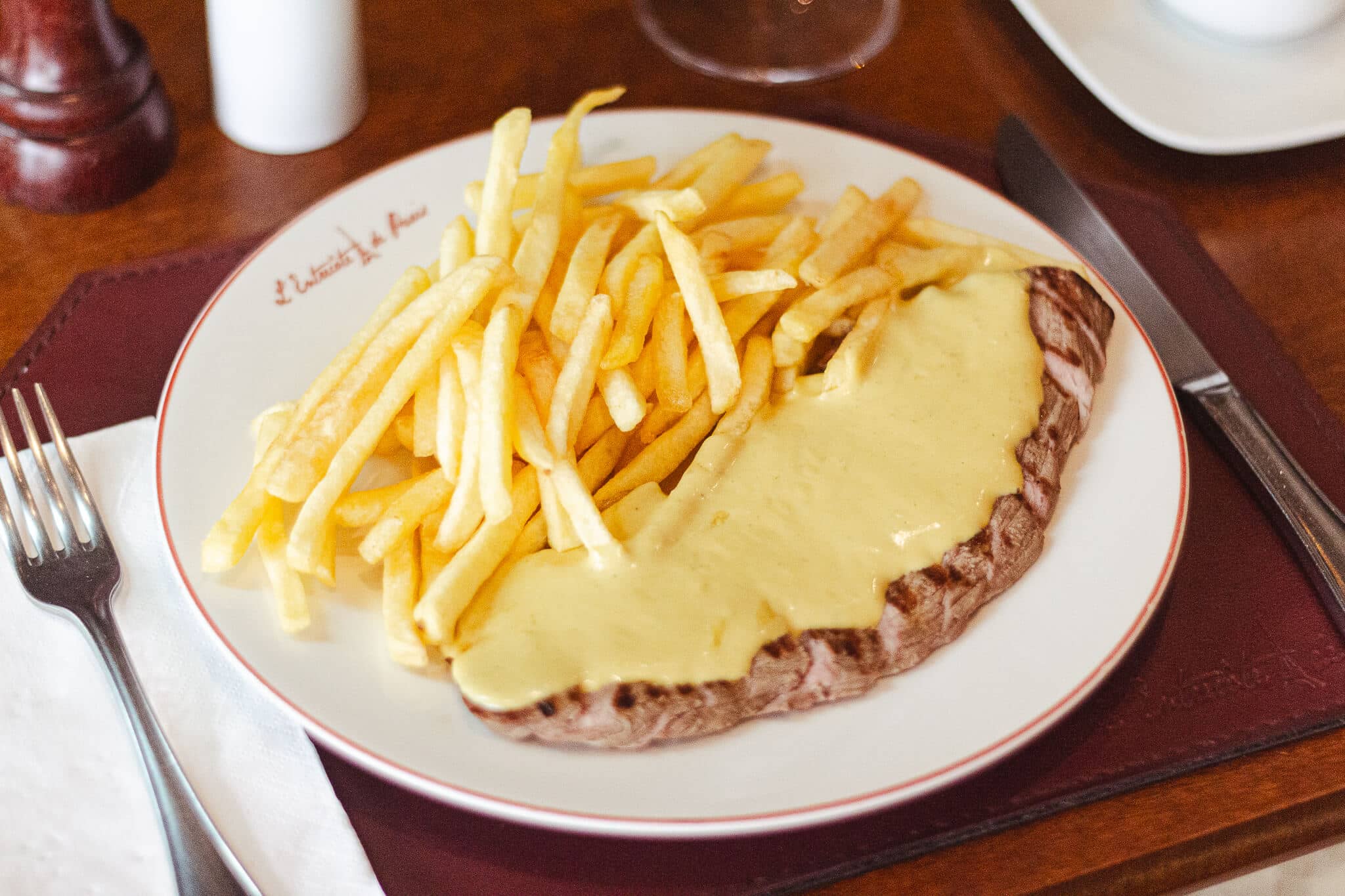 foto mostra o prato com entrecote e batata frita com um molho secreto amarelo por cima da carne