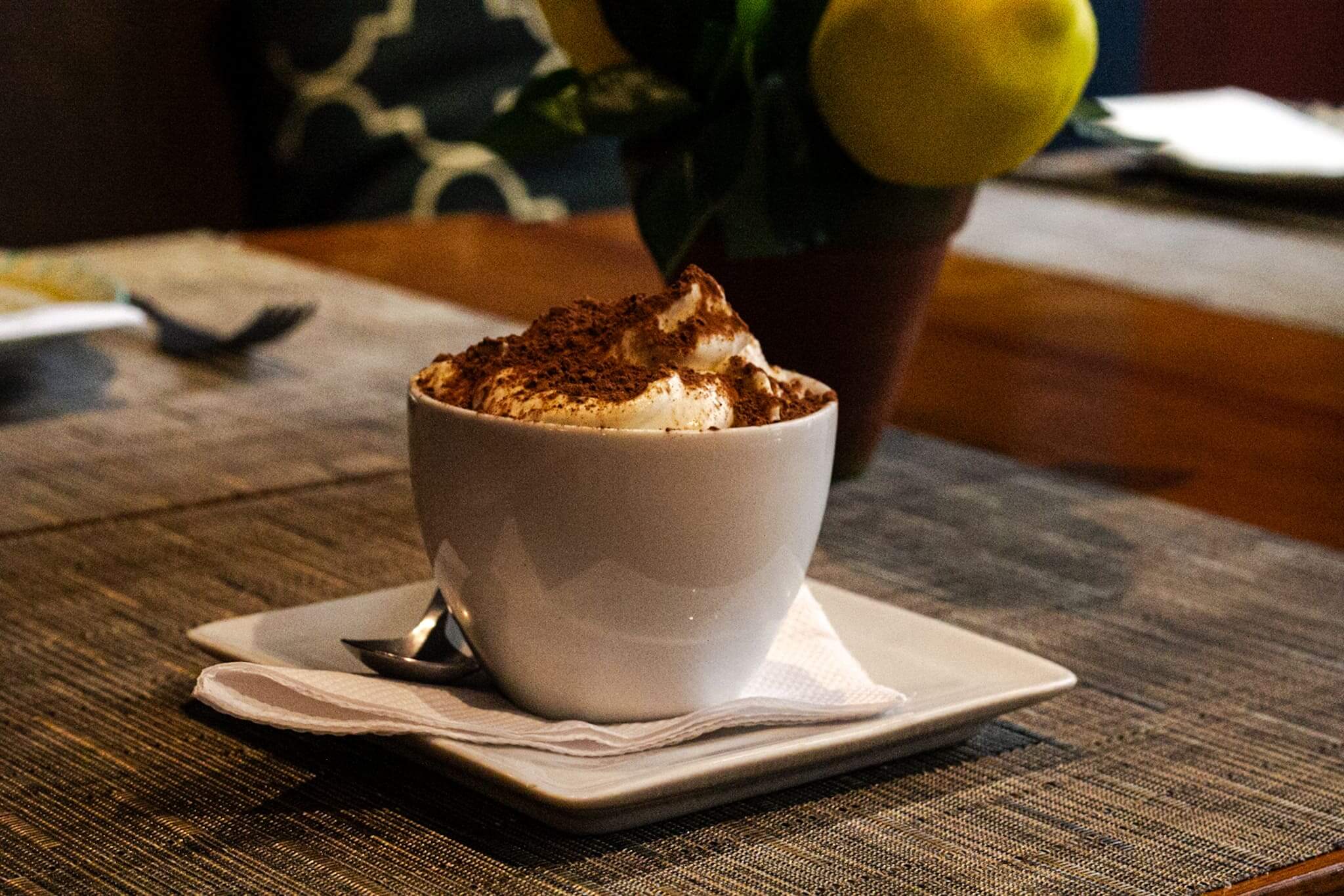 A foto mostra uma xícara branca com um Tiramisú Espresso do Pina. Essa sobremesa combina camadas de biscoitos embebidos em café expresso, creme de queijo mascarpone e cacau em pó.