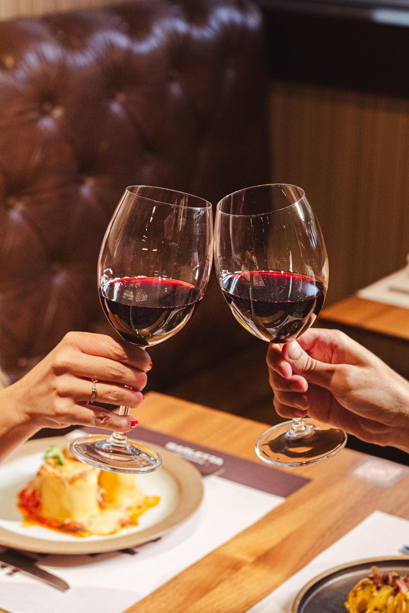 foto mostra duas pessoas brindando com taças de vinho, ao fundo está as massas: coliseu e spaghetti